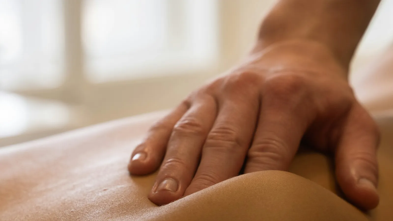 Mains d'ostéopathe posées avec douceur sur le dos d'un patient allongé