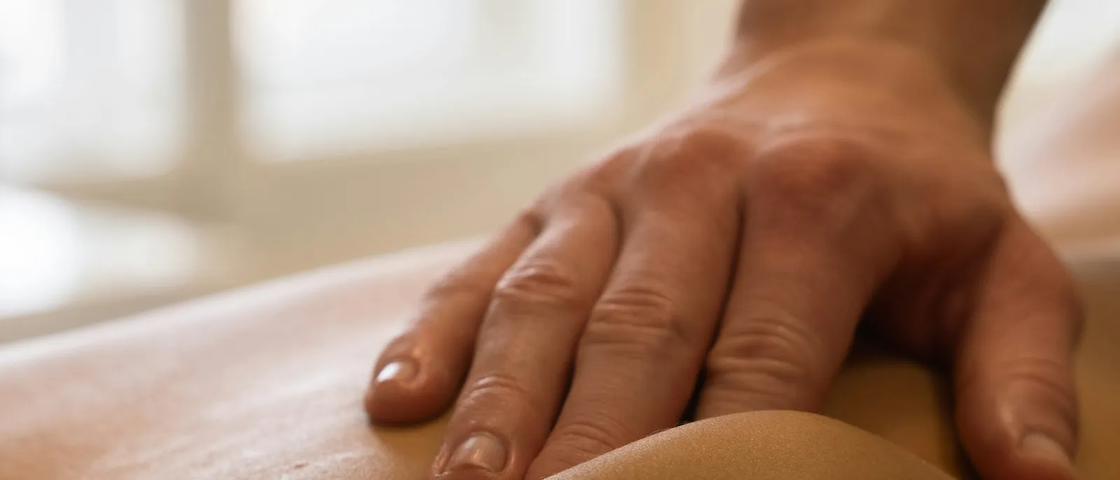 Mains d'ostéopathe posées avec douceur sur le dos d'un patient allongé